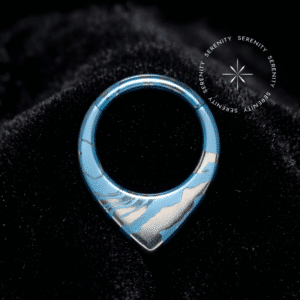 Piercing Argola Septo Titânio repousando suavemente sobre um veludo de seda preto de alta opulência, destacando o formato em V e a textura marmorizada azul e prata.