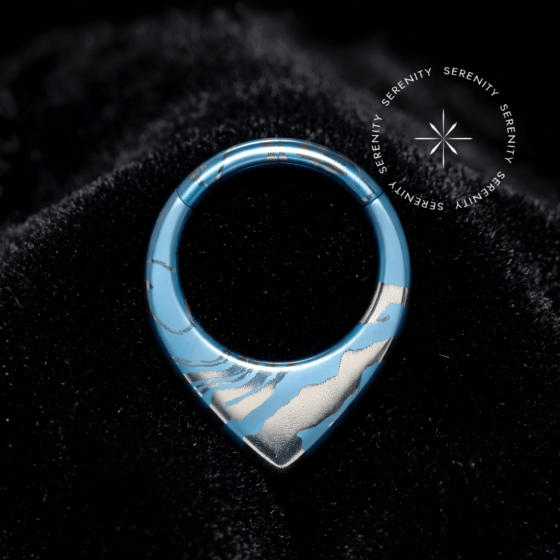 Piercing Argola Septo Titânio repousando suavemente sobre um veludo de seda preto de alta opulência, destacando o formato em V e a textura marmorizada azul e prata.