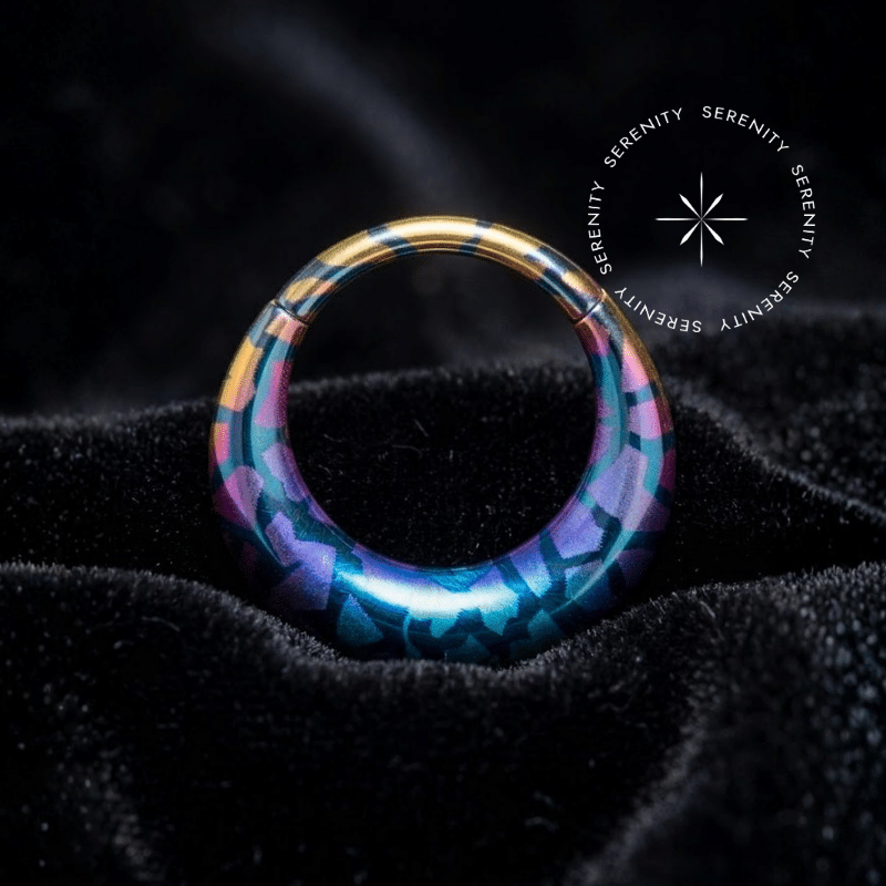 Piercing Argola Septo Titânio repousando suavemente sobre um tecido de cetim preto de alta opulência, destacando o formato oval e a estampa de serpente em tons boreais iridescentes.