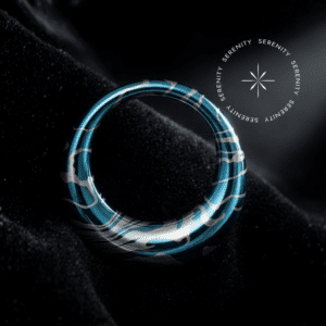 Piercing Argola Septo Titânio repousando suavemente sobre um tecido de cetim preto de alta opulência, destacando o formato oval abaulado e a textura fluida em tons de azul e prata.