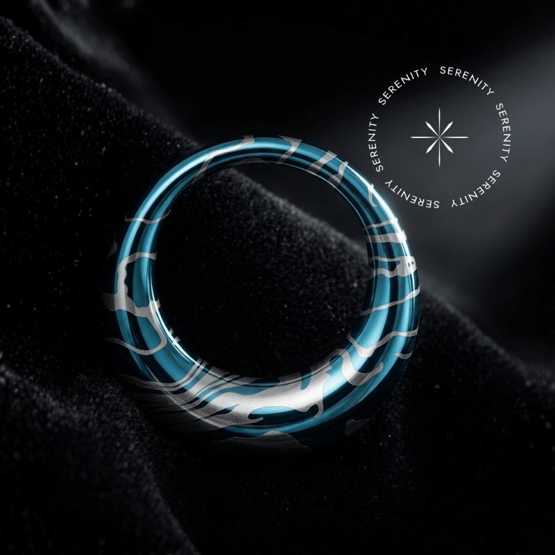 Piercing Argola Septo Titânio repousando suavemente sobre um tecido de cetim preto de alta opulência, destacando o formato oval abaulado e a textura fluida em tons de azul e prata.