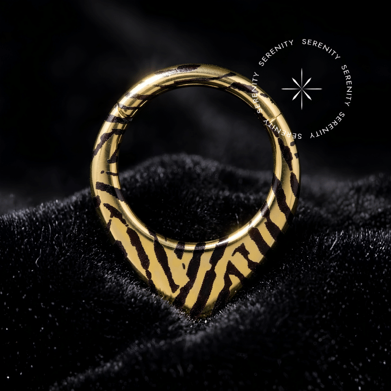 Piercing Argola Septo Titânio repousando suavemente sobre um veludo de seda preto de alta opulência, destacando o formato em V e a estampa listrada contrastante.