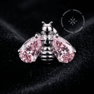 piercing titânio grau implante com design de abelha esculpida, adornado por duas asas de zircônia rosa em lapidação gota, repousando suavemente sobre um tecido de cetim branco de alta opulência.
