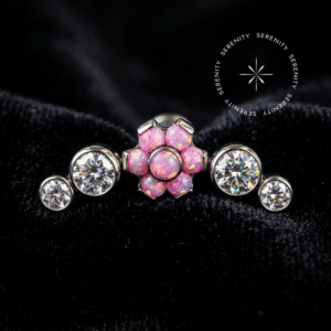 piercing titânio grau implante com design em cluster de 14mm adornado por flor central de opalas rosa e magenta e zircônias translúcidas laterais, repousando suavemente sobre um tecido de cetim branco de alta opulência.