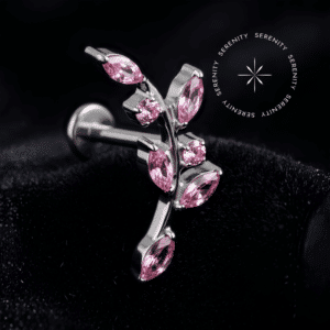 Piercing Topo de Orelha Titânio repousando suavemente sobre um tecido de cetim preto de alta opulência, destacando o formato de ramo com zircônias cor rosa e o brilho do metal.