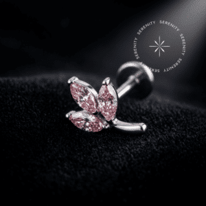 Topo Mini Folhas Cravejado em Titânio com três zircônias rosas de lapidação premium cravadas em metal polido, repousando suavemente sobre um tecido de cetim branco de alta opulência.