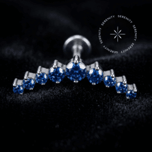 Labret Cluster Curvo Cravejado em Titânio com zircônias azuis repousando suavemente sobre um tecido de cetim branco de alta opulência, destacando o polimento impecável e o design anatômico da peça.