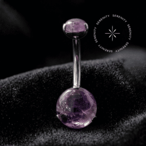 piercing de umbigo titânio repousando suavemente sobre um tecido de cetim branco de alta opulência, destacando o polimento profundo do titânio e os tons roxos da gema natural.