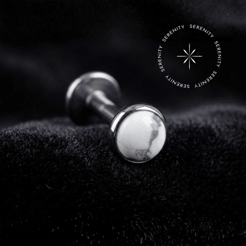 piercing topo pedra natural branca titânio repousando suavemente sobre um tecido de cetim branco de alta opulência, destacando o polimento profundo do titânio e o contraste da gema.