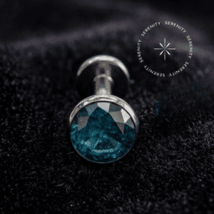 Piercing Topo para Labret em Titânio repousando suavemente sobre um tecido de cetim branco de alta opulência, destacando o polimento profundo e a gema turquesa.