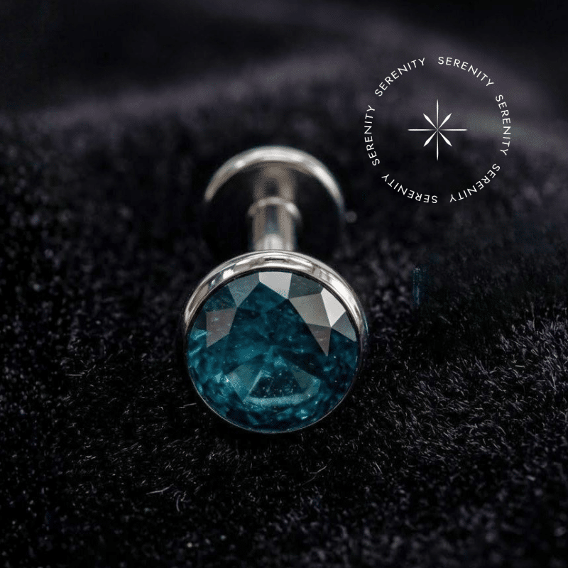 Piercing Topo para Labret em Titânio repousando suavemente sobre um tecido de cetim branco de alta opulência, destacando o polimento profundo e a gema turquesa.