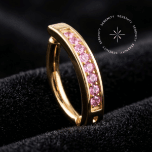 Piercing Umbigo Argola Titânio Dourado repousando suavemente sobre um tecido de cetim preto de alta opulência, destacando o contraste do ouro com a fileira de pedrarias vivas.