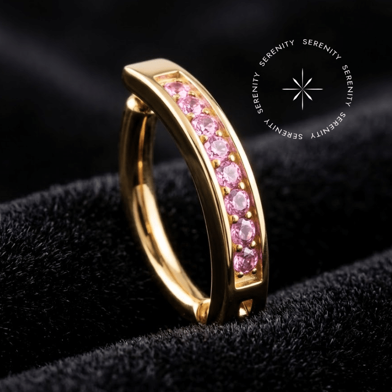Piercing Umbigo Argola Titânio Dourado repousando suavemente sobre um tecido de cetim preto de alta opulência, destacando o contraste do ouro com a fileira de pedrarias vivas.