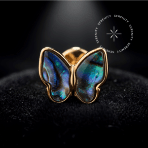 piercing pedra natural titanio repousando suavemente sobre um tecido de cetim preto de alta opulência, destacando sua silhueta de borboleta e o brilho iridescente da gema orgânica abalone.