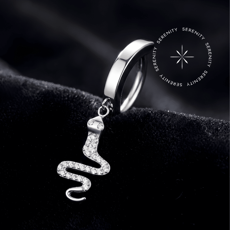 Piercing Umbigo Serpente Titânio repousando suavemente sobre um tecido de cetim branco de alta opulência, evidenciando o pingente de cobra cravejado e o polimento espelhado do metal.