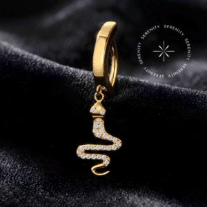 Piercing Umbigo Serpente Titânio Dourado repousando suavemente sobre um tecido de cetim preto de alta opulência, destacando o pingente de cobra cravejado e o revestimento em ouro 18k.
