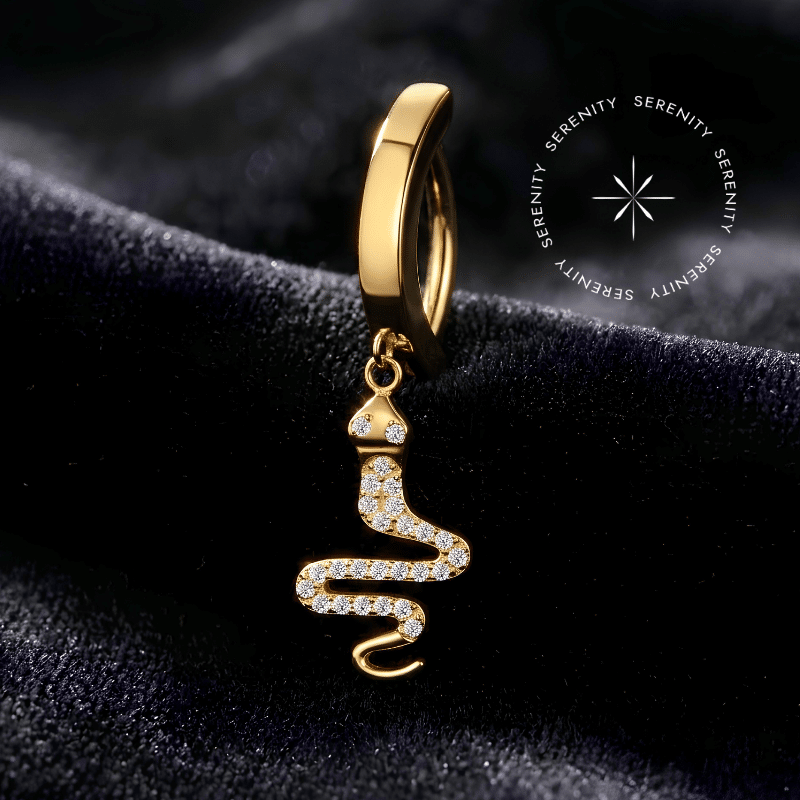 Piercing Umbigo Serpente Titânio Dourado repousando suavemente sobre um tecido de cetim preto de alta opulência, destacando o pingente de cobra cravejado e o revestimento em ouro 18k.