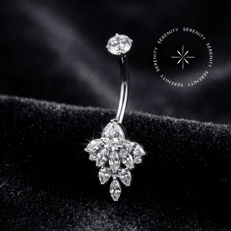 Piercing Umbigo Titânio repousando suavemente sobre um tecido de cetim branco de alta opulência, evidenciando o cluster floral inferior finamente cravejado com zircônias translúcidas.