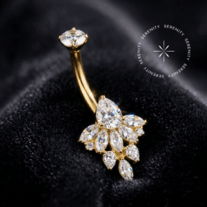 Piercing Umbigo Titânio Dourado repousando suavemente sobre um tecido de cetim preto de alta opulência, evidenciando o cluster floral inferior finamente cravejado com zircônias translúcidas.