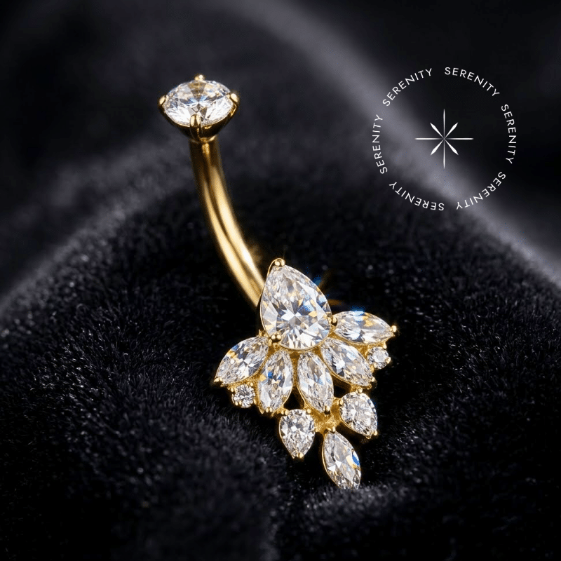 Piercing Umbigo Titânio Dourado repousando suavemente sobre um tecido de cetim preto de alta opulência, evidenciando o cluster floral inferior finamente cravejado com zircônias translúcidas.