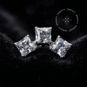 Topo Piercing Titânio Cravejado com três zircônias translúcidas quadradas brilhantes, estrutura espelhada, repousando suavemente sobre um tecido de cetim branco de alta opulência.