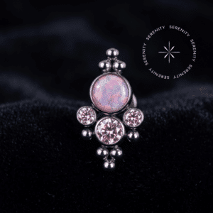 Topo Opala e Zircônias Cravejado Titânio exibindo uma pedra central opalescente rosa e três zircônias de lapidação premium na cor rosa, repousando suavemente sobre um tecido de cetim branco de alta opulência.