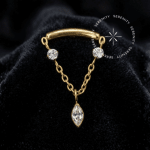 Piercing Topo Corrente em Titânio com polimento espelhado impecável e zircônias de lapidação premium, capturando a luz em um ambiente de alto luxo, apresentando um arco estrutural dourado conectado a uma delicada corrente pendente com três gemas navete.